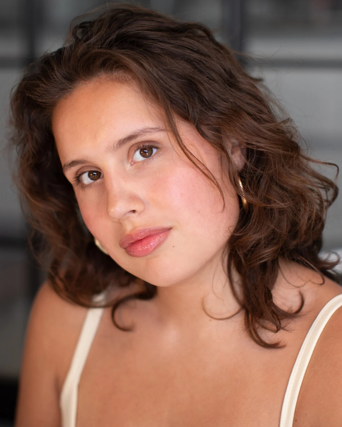 Anastasia Borodina, actor, head-and-shoulders portrait in a cream tank top, warm natural light, looking directly at camera with a slight head tilt.