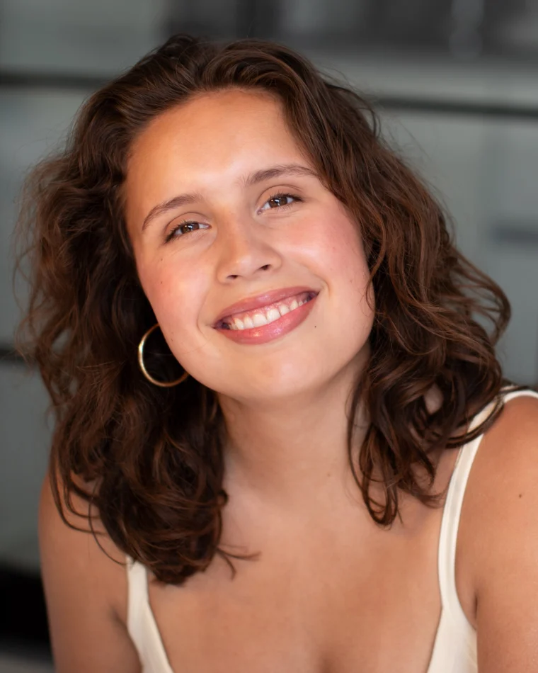 Anastasia Borodina, actor, head-and-shoulders portrait in a cream tank top, laughing with an open smile.
