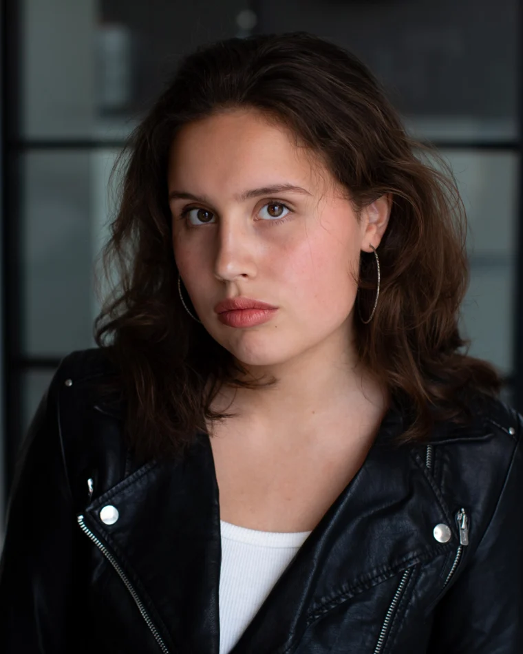 Anastasia Borodina, actor, head-and-shoulders portrait in a black leather jacket over a white top, still and direct, looking straight at camera.